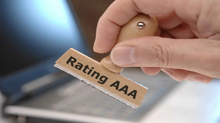 Obrazek przedstawia rękę trzymająca stempel z napisem „Rating AAA”. Symbolizuje to najwyższą ocenę kredytową nadawaną przez agencje ratingowe.